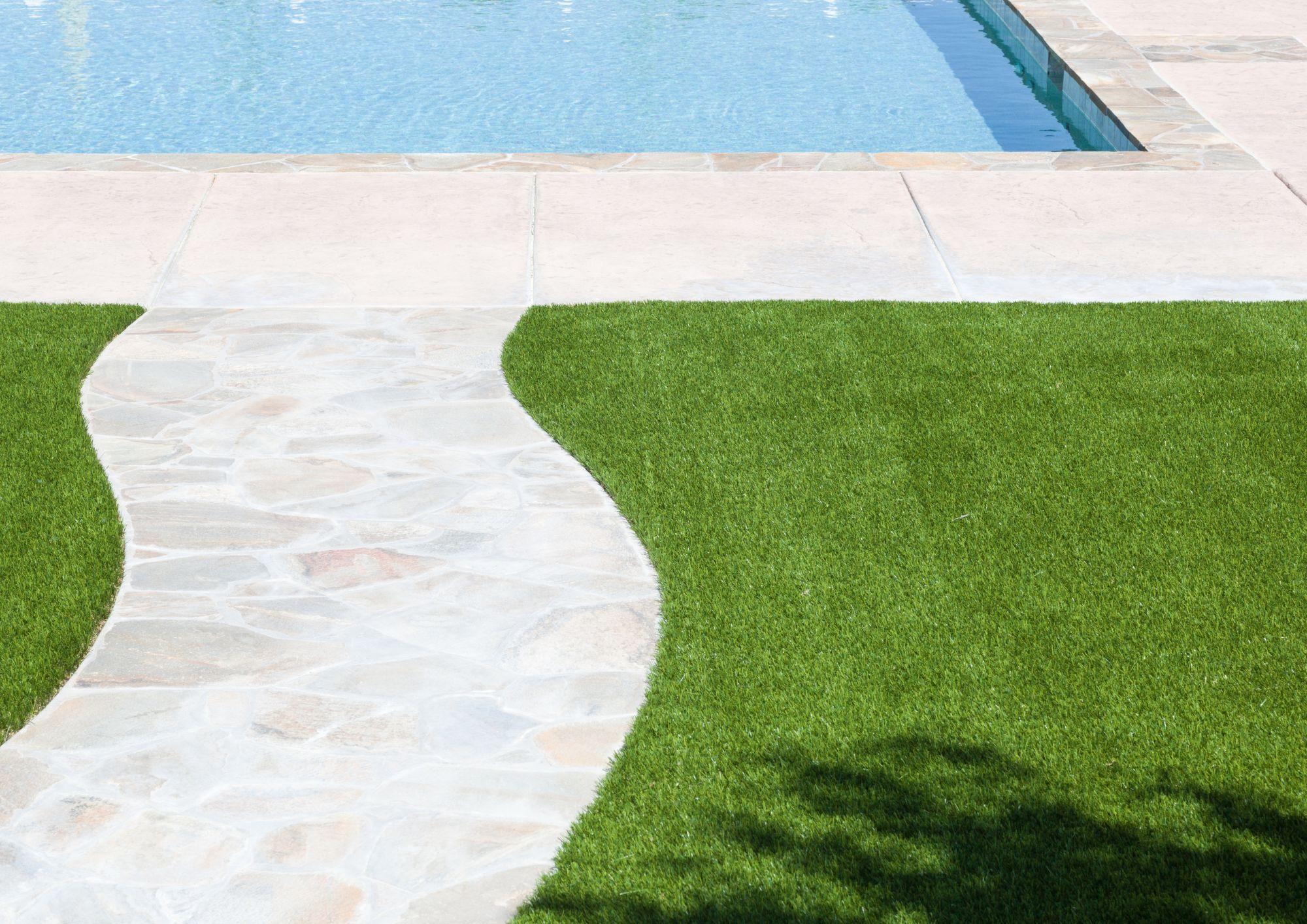 Patio con un camino y una piscina de fondo sobre un cesped artificial